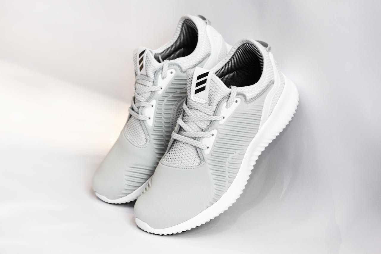 digital Pair of sports shoes with gray dense texture of surface and rubber inserts from sided and laces and white soles placed with heels up leaning on glance gray background