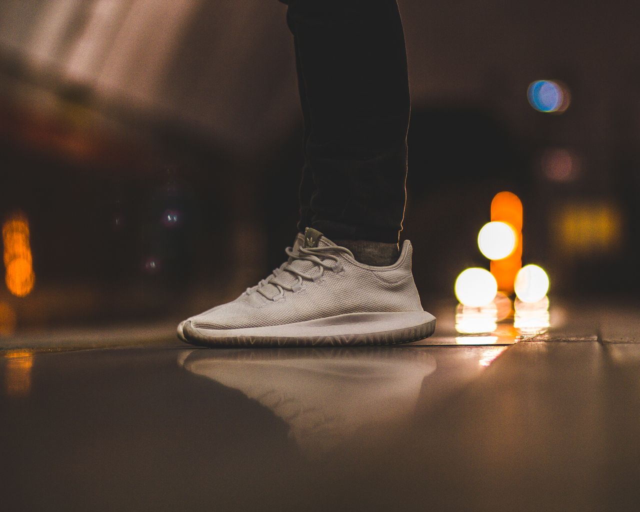Services-02 Close-up of white sneakers on a reflective surface with urban night lights creating a bokeh effect.
