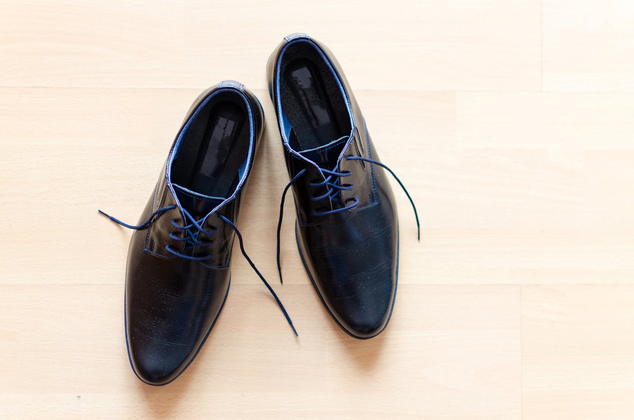 digital-01 Pair of stylish black leather shoes with blue laces on a wooden floor.