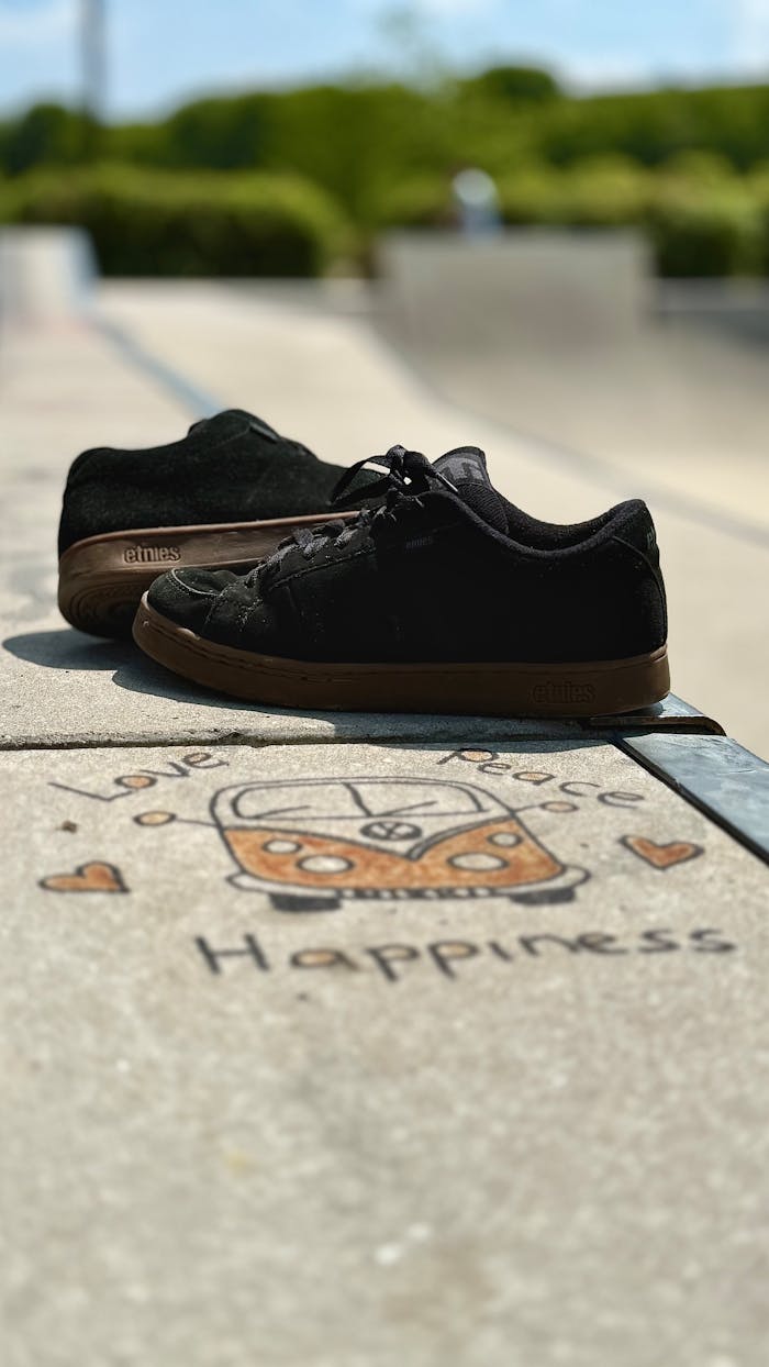 Services-03 Black casual sneakers resting on sidewalk with artistic design symbolizing peace and happiness.