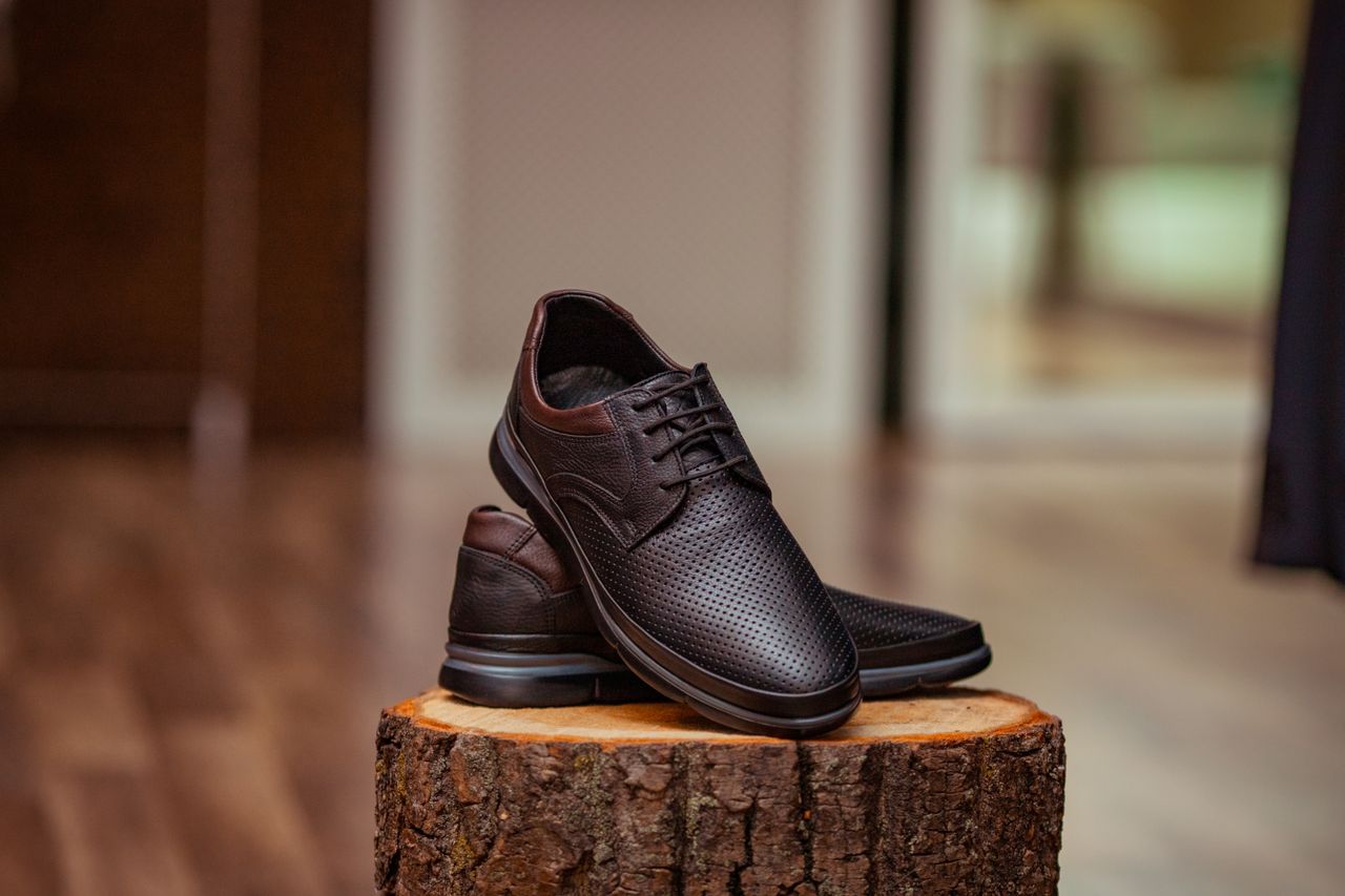 why-choose-us Stylish perforated leather shoes displayed elegantly on a rustic wooden stump indoors.